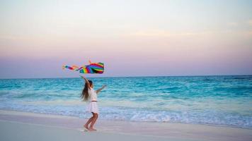 aanbiddelijk weinig meisje met vliegend vlieger Aan tropisch strand Bij zonsondergang. kinderen Speel Aan oceaan oever. kind met strand speelgoed.