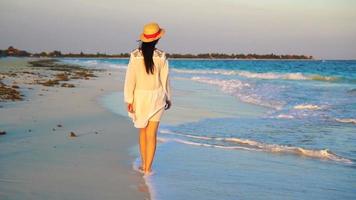 ung skön kvinna på tropisk havsstrand i solnedgång. Lycklig flicka i klänning i de kväll på de strand. långsam rörelse video