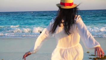 vista traseira da mulher bonita na praia tropical no pôr do sol, apreciando a vista para o mar. garota feliz no vestido em câmera lenta video