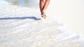 Nahaufnahmebeine, die im seichten Wasser am weißen Strand entlang laufen. konzept von strandurlaub und barfuß. Zeitlupe. video