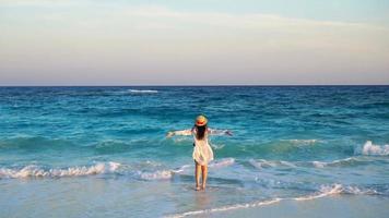 vista trasera de una mujer hermosa con sombrero en las vacaciones de verano en la playa blanca. chica feliz disfruta de la vista al mar en cámara lenta video