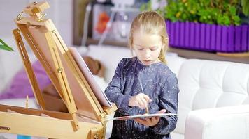 adorable niña pintando un cuadro en caballete interior video