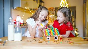 niñas pequeñas haciendo casa de pan de jengibre de navidad en la chimenea en la sala de estar decorada. video