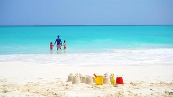 castello di sabbia a bianca spiaggia con plastica bambini giocattoli e famiglia nel il mare sfondo video