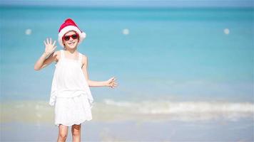 Little adorable girl in Christmas hat on white beach having fun on Xmas vacation video