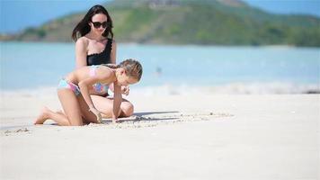 Mother and her little daughter enjoying Caribbean beach vacation. Family playing with sand on tropical beach video