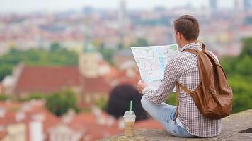 joven con un mapa de la ciudad y una mochila de fondo ciudad europea. turista caucásico mirando el mapa de la ciudad europea con hermosas vistas de las atracciones. video