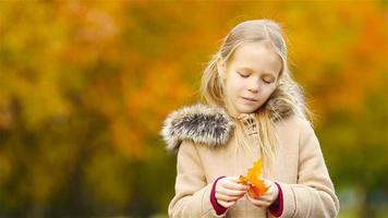 portrait d'une adorable petite fille à l'extérieur lors d'une belle journée chaude avec une feuille jaune à l'automne video