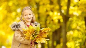 Porträt eines entzückenden kleinen Mädchens mit gelben und orangefarbenen Blättern im Freien an einem schönen Herbsttag