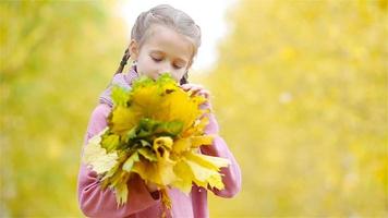 Porträt eines entzückenden kleinen Mädchens mit gelben und orangefarbenen Blättern im Freien an einem schönen Herbsttag