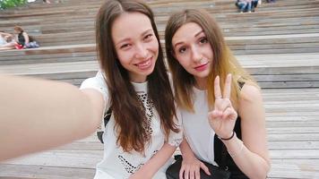 Beautiful happy girls smile and making selfie. Young tourist friends traveling on holidays outdoors smiling happy. video
