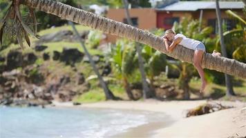 adorable petite fille assise sur un palmier pendant les vacances d'été sur la plage blanche video