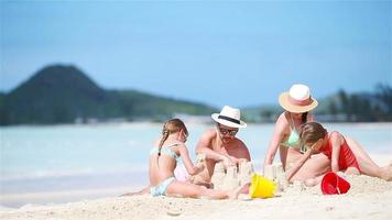 familia de cuatro haciendo castillos de arena en la playa blanca tropical video