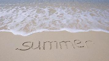 Word Summer handwritten on sandy beach with soft ocean wave on background video