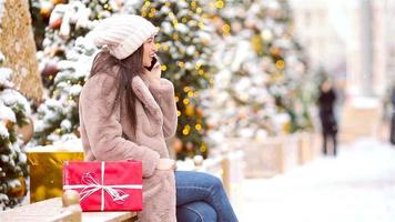 Cute woman is reading text message on mobile phone while sitting in the park. video