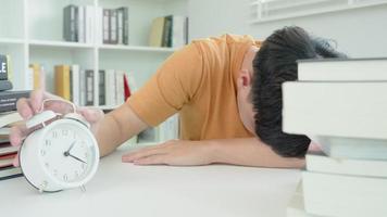 Asian student man turns off the alarm clock because he is tired from reading, male prepare for test and learning lessons in the library. stress, despair, haste, misunderstanding reading, discouraged.