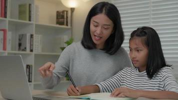 Curso en línea de tutor en línea para niños asiáticos. videoconferencia en la computadora portátil en casa. Reproduzca el curso en línea, las estudiantes usan auriculares para estudiar, anotan tareas, clases de video, nueva educación. video