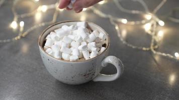 Marshmallows in a mug with a hot drink sprinkle chocolate chips. Lights are on in the background. Slow motion video