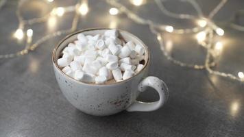 Marshmallows in a mug with a hot drink sprinkle chocolate chips. Lights are on in the background. Slow motion video