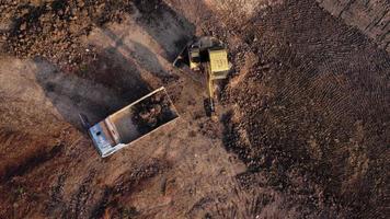 antenn se av en hjul lastare grävmaskin med en traktor läser in sand in i en tung earthmover på en konstruktion webbplats. grävmaskin grävning jord gropar för de jordbruks industri. video