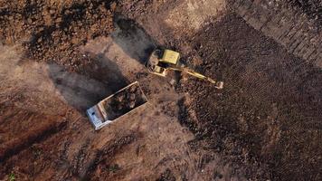 antenn se av en hjul lastare grävmaskin med en traktor läser in sand in i en tung earthmover på en konstruktion webbplats. grävmaskin grävning jord gropar för de jordbruks industri. video