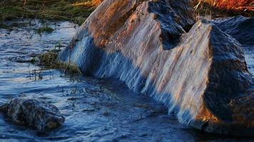 la ola del mar rueda en la orilla y se rompe en un bloque de granito, a cámara lenta video