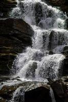 Cascading down a small mountain stream, the water runs over basalt boulders. A small waterfall runs through the moss. photo