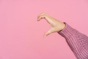 Young woman forming shape of half of heart with her fingers isolated on pink background with copy space. photo