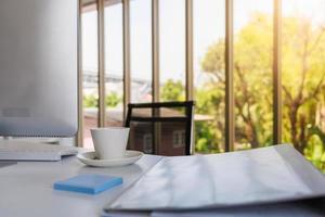 vista de la sala de oficina, primer plano de una taza blanca de café caliente con computadora de escritorio, teclado, carpeta de documentos y notas en papel con espacio para copiar. foto