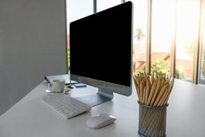 View of office room computer desktop with blank screen copyspace, keyboard, mouse,  white cup of coffee and pencil. Using as Business and work concept. photo