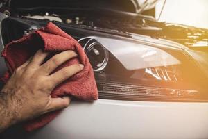 Hand is cleaning car headlight with a using red microfiber cloth Automotive maintenance service concept photo