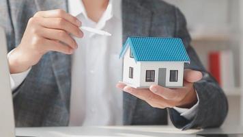 agente de corretaje de bienes raíces entrega una muestra de una casa modelo al cliente, contrato de préstamo hipotecario que arrienda y compra y vende casa y contrata el concepto de préstamo hipotecario de seguro de hogar