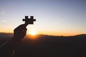 silueta de la mano de una mujer sosteniendo una pieza de rompecabezas contra el amanecer, soluciones comerciales, targsilhouette de una mano de mujer de negocios sosteniendo una pieza de rompecabezas contra el amanecer, soluciones comerciales. foto