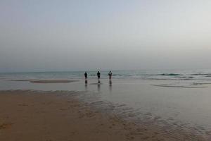 lonely beach with people strolling on the sand at the edge of the sea waves photo