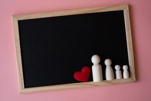 figuras de madera de padre de familia, madre e hijos en el tablero negro sobre fondo rosa. copie el espacio para el texto. foto