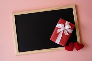 Red gift box and red heart shape on the black board isolated on pink background. photo