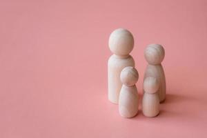 Wooden figurines of family father, mother and children on pink background. A warm family concept. photo