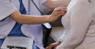 Homecare nursing service and elderly people cardiology healthcare. Close up of young hispanic female doctor nurse check mature caucasian man patient heartbeat using stethoscope during visit photo