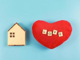 flat layout of wooden model house and red heart shape pillow with wooden letters L O V E  isolated  on blue  background with copy space, valentines or home of love concept. photo