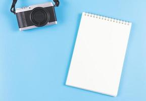 endecha plana de cuaderno abierto de página en blanco y cámara sobre fondo azul. foto