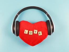 endecha plana de almohada de corazón rojo con amor de letras de madera cubierto con auriculares sobre fondo azul. canciones de amor, podcast o concepto de San Valentín. foto