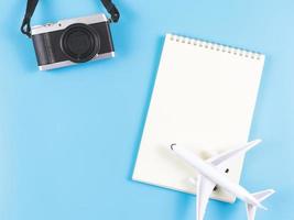 endecha plana de cuaderno abierto de página en blanco, modelo de avión y cámara sobre fondo azul. foto