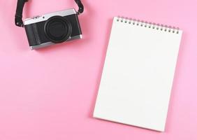flat lay of blank page opened notebook and camera on pink  background with copy space. photo