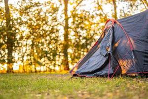 Camping tent in the forest with sunset and beautiful blurred nature scenery. Trees and sun rays in summer spring park. Hiking as recreational activity, outdoor nature forest scene