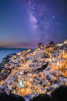 Oia village in sunset light with stars and milky way, Santorini, Greece. Amazing summer vacation landscape, white architecture and evening lights. Famous travel destination, urban travel background photo
