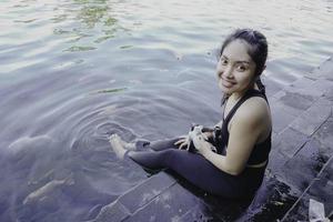 Attractive young woman sitting by the edge of a swimming pool, holding a google photo