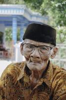 A portrait of an old Asian man wearing batik shirt and glasses photo