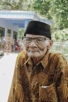 A portrait of an old Asian man wearing batik shirt and glasses photo