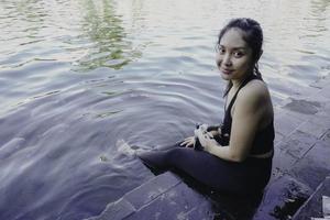 Attractive young woman sitting by the edge of a swimming pool, holding a google photo