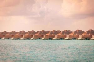 increíble panorama de puesta de sol en maldivas. villas de lujo en el paisaje marino con un cielo suave y colorido. destino de viaje tropical para vacaciones de verano o vacaciones, filas de bungalows de agua foto